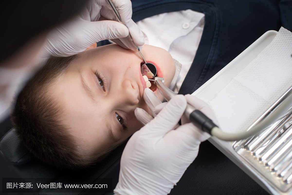 开放嘴的男孩在钻治疗期间在牙科诊所的小儿科