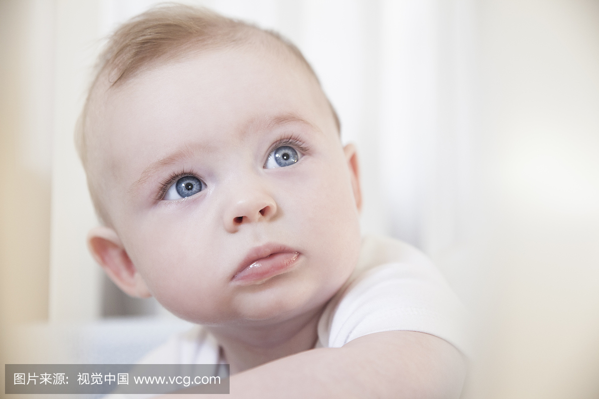 从婴儿床盯着的蓝眼睛的男婴的肖像
