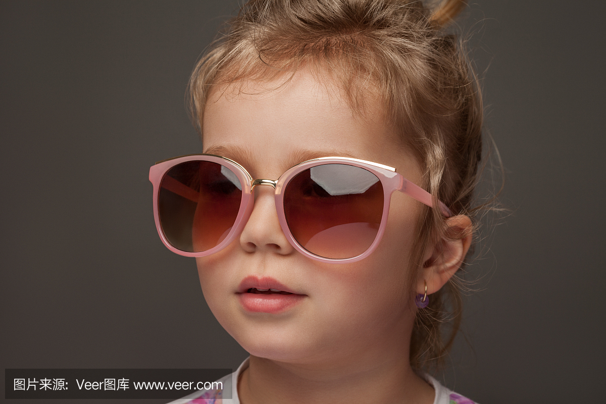 戴墨镜的可爱小女孩在灰色的背景上