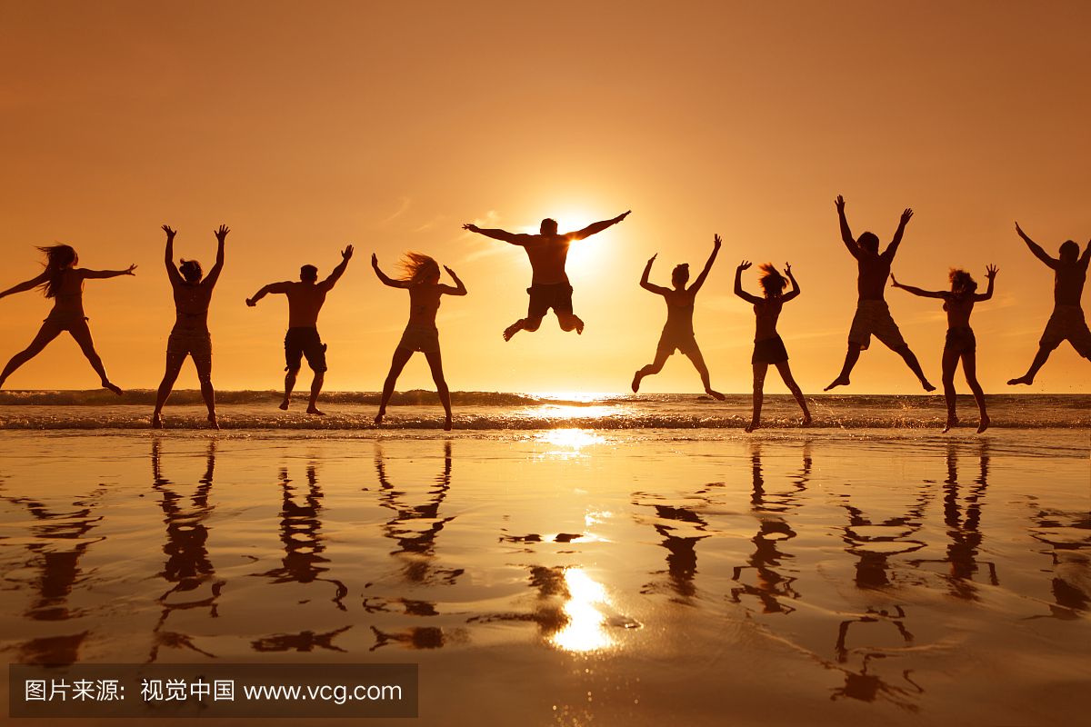 年轻的大人在日落时在海滩上空中跳跃