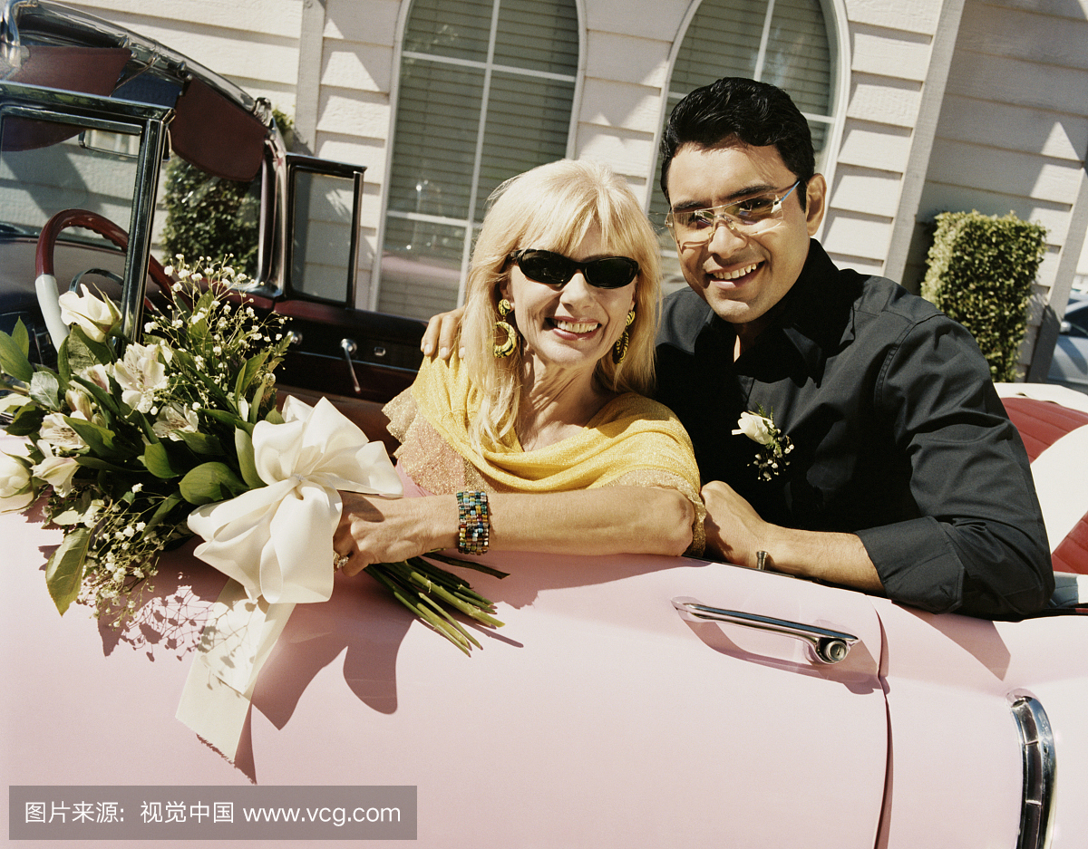 坐在粉红色的1950年代风格的汽车的新婚夫妇