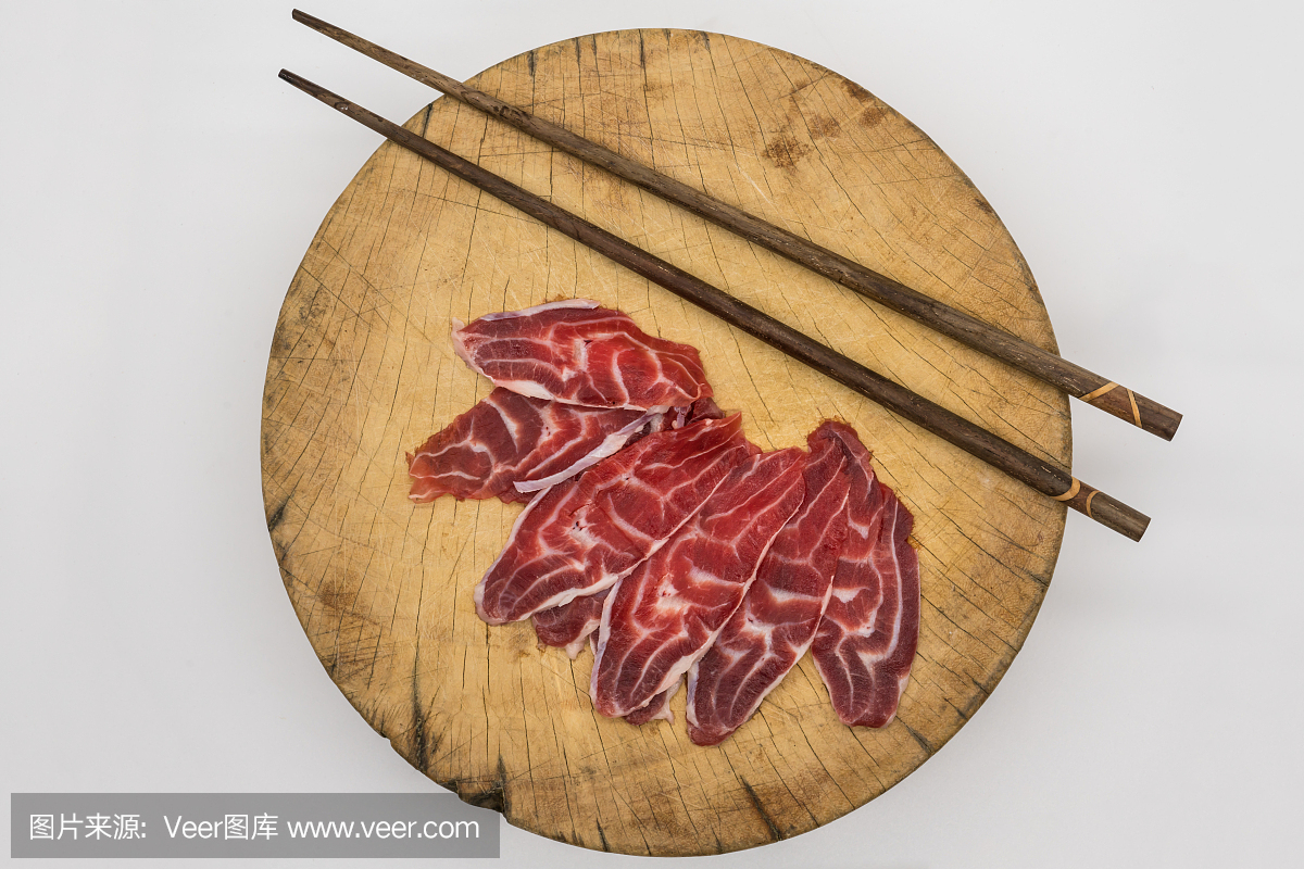 在木砧板上用新鲜切片牛肉后腿用筷子孤立在白