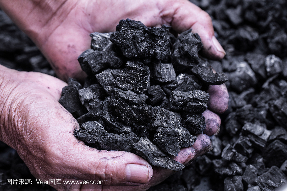 煤矿开采 - 拿着自然黑木炭为背景的人手。关于