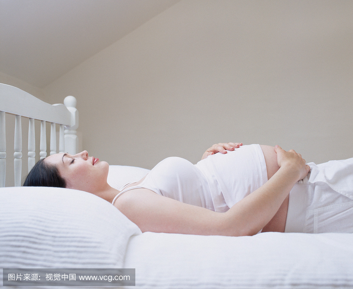 躺在床上的年轻孕妇,触摸胃,侧视图