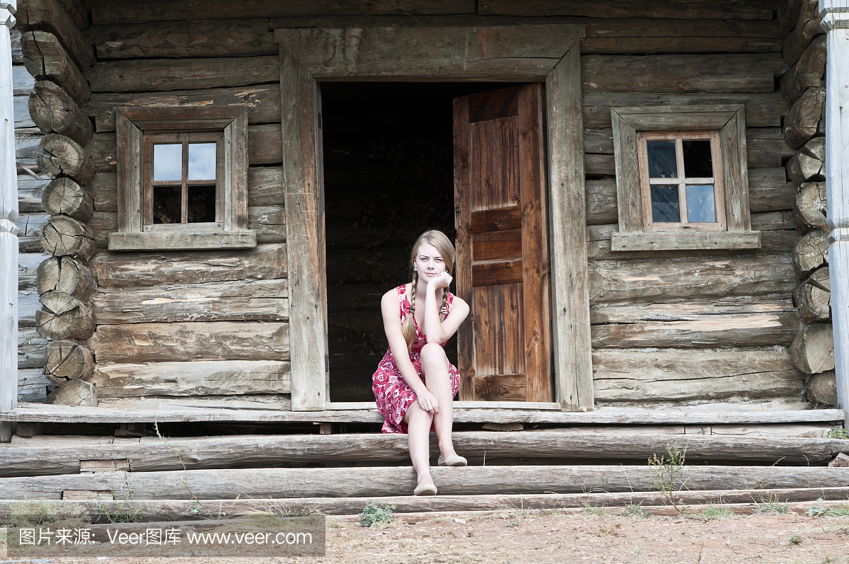 乡下女孩坐在老木房子的门廊上