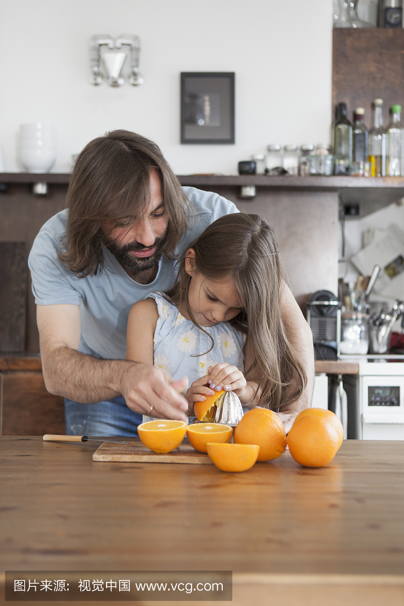 父亲帮助女儿在家中从榨汁机上挤出桔子