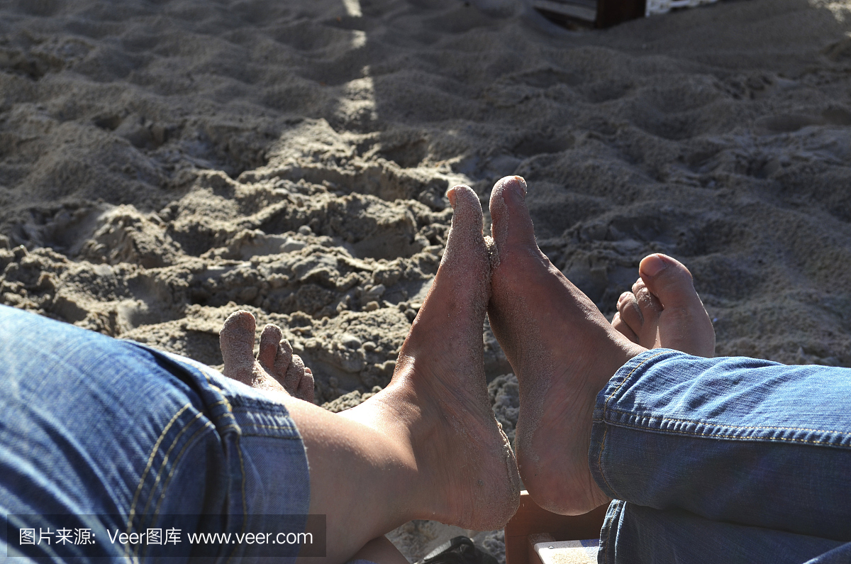 一对夫妇在赤脚坐在沙滩椅上的牛仔裤的腿