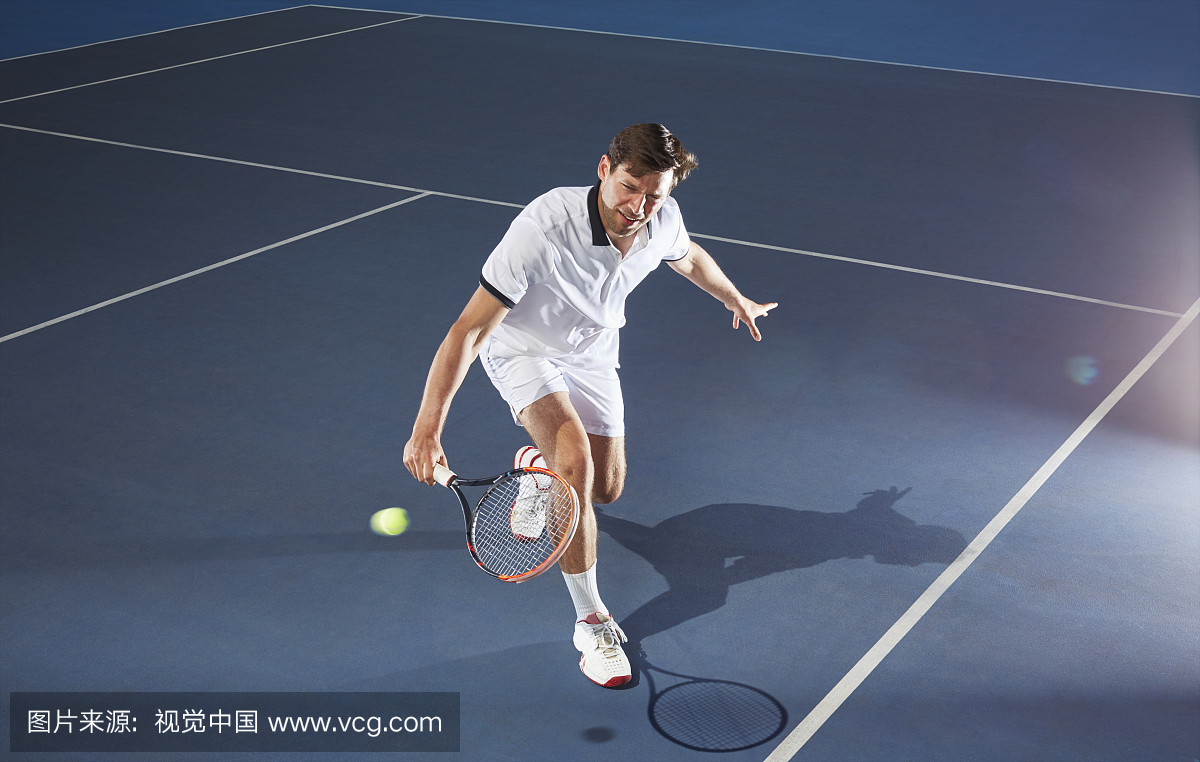 年轻的男网球运动员打网球,达到与网球拍在蓝