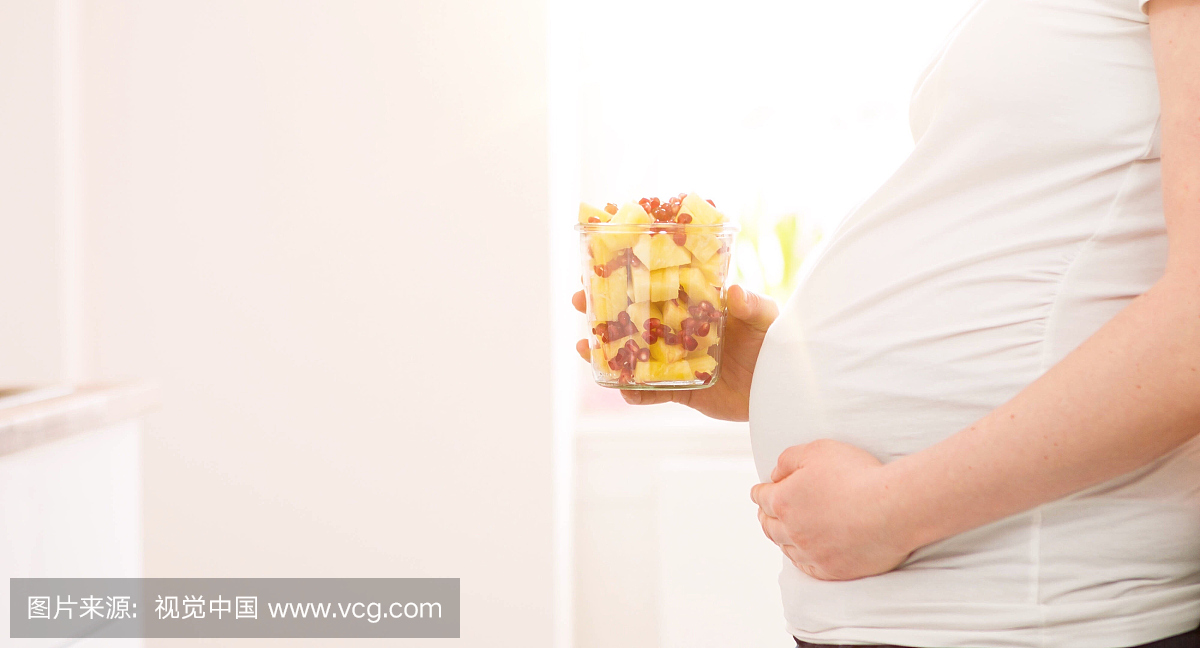 怀孕的女人拿着玻璃与水果在家里面