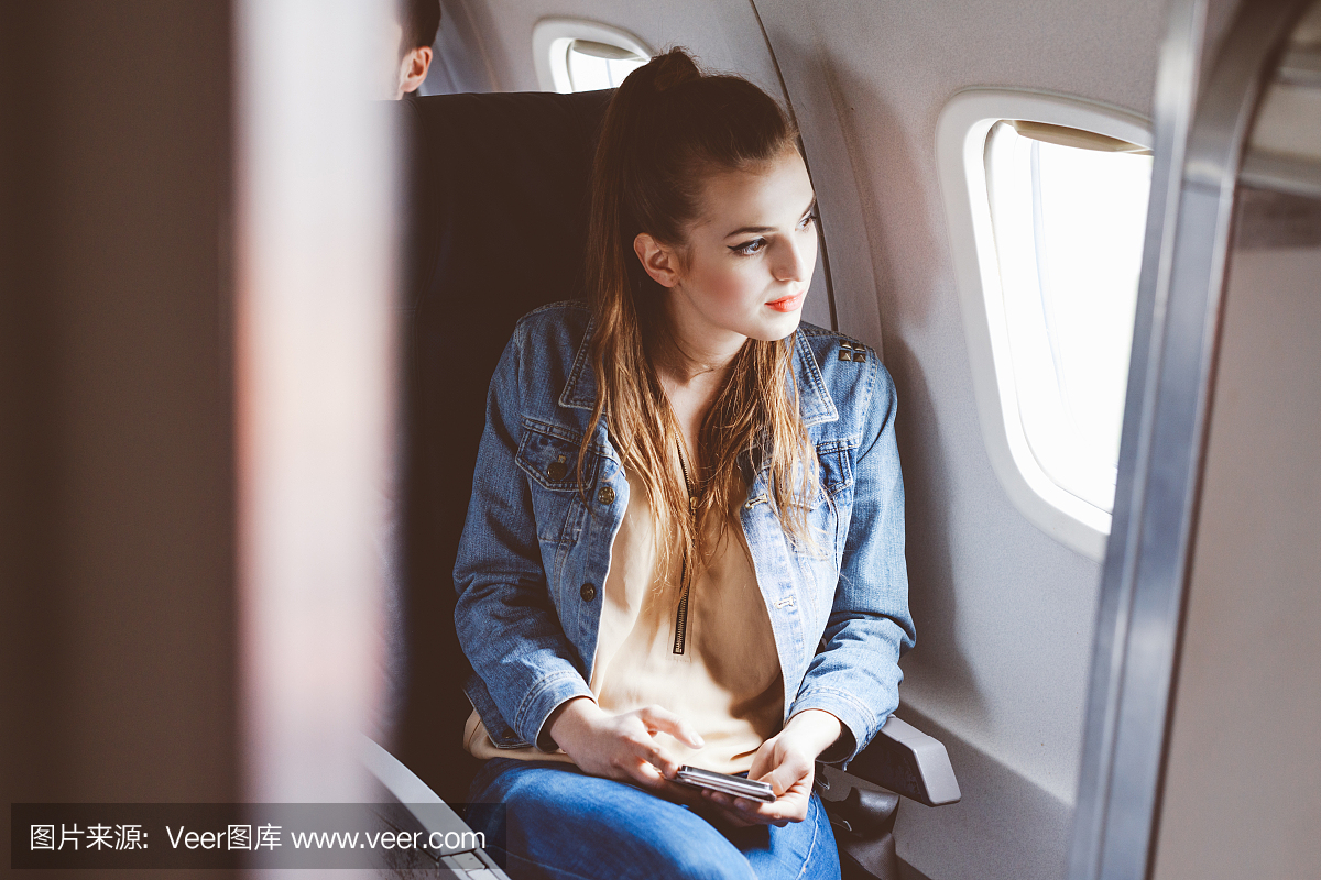 坐在飞机舱附近的年轻女子在窗口附近