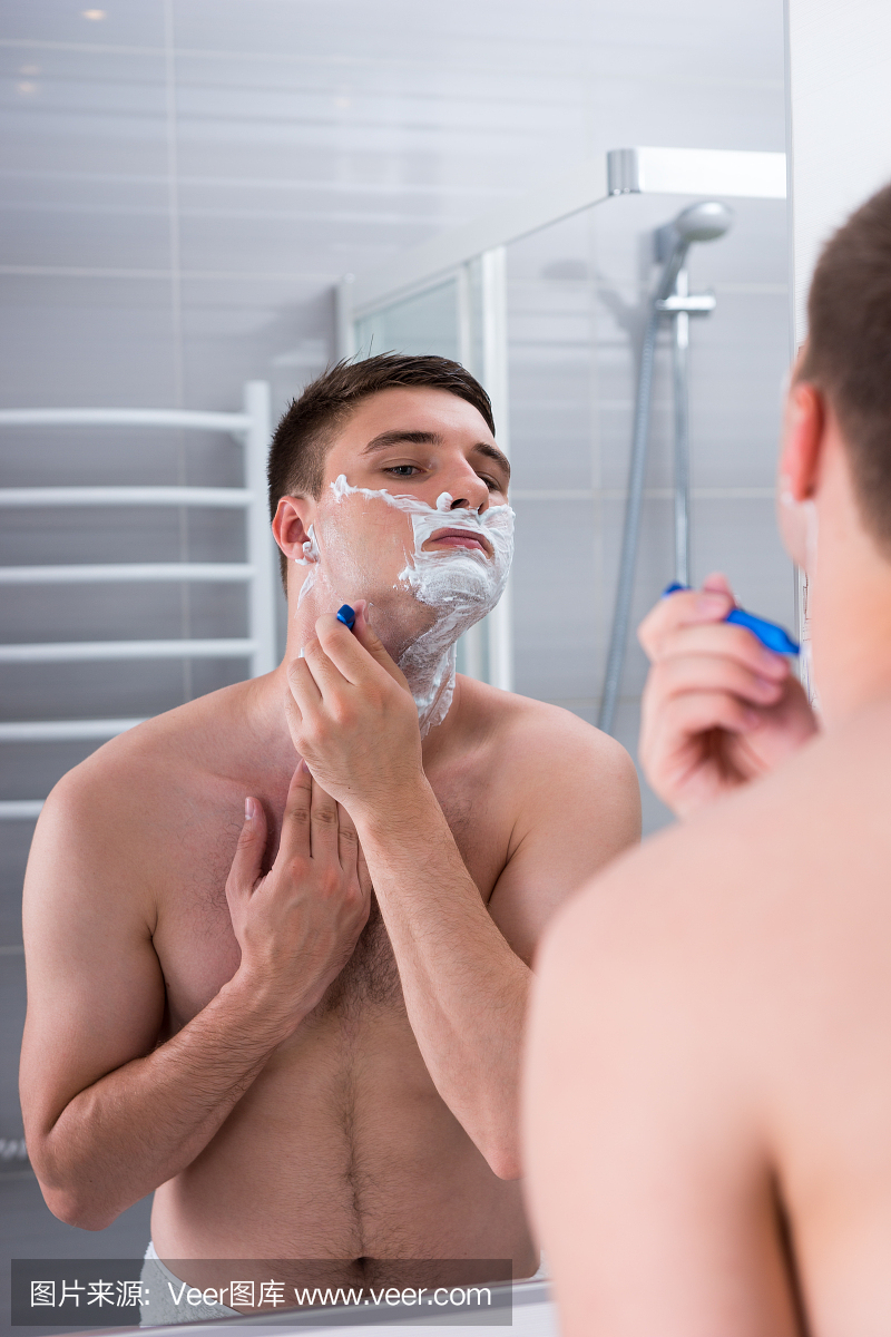 男人用剃须刀刮脸,看着镜子