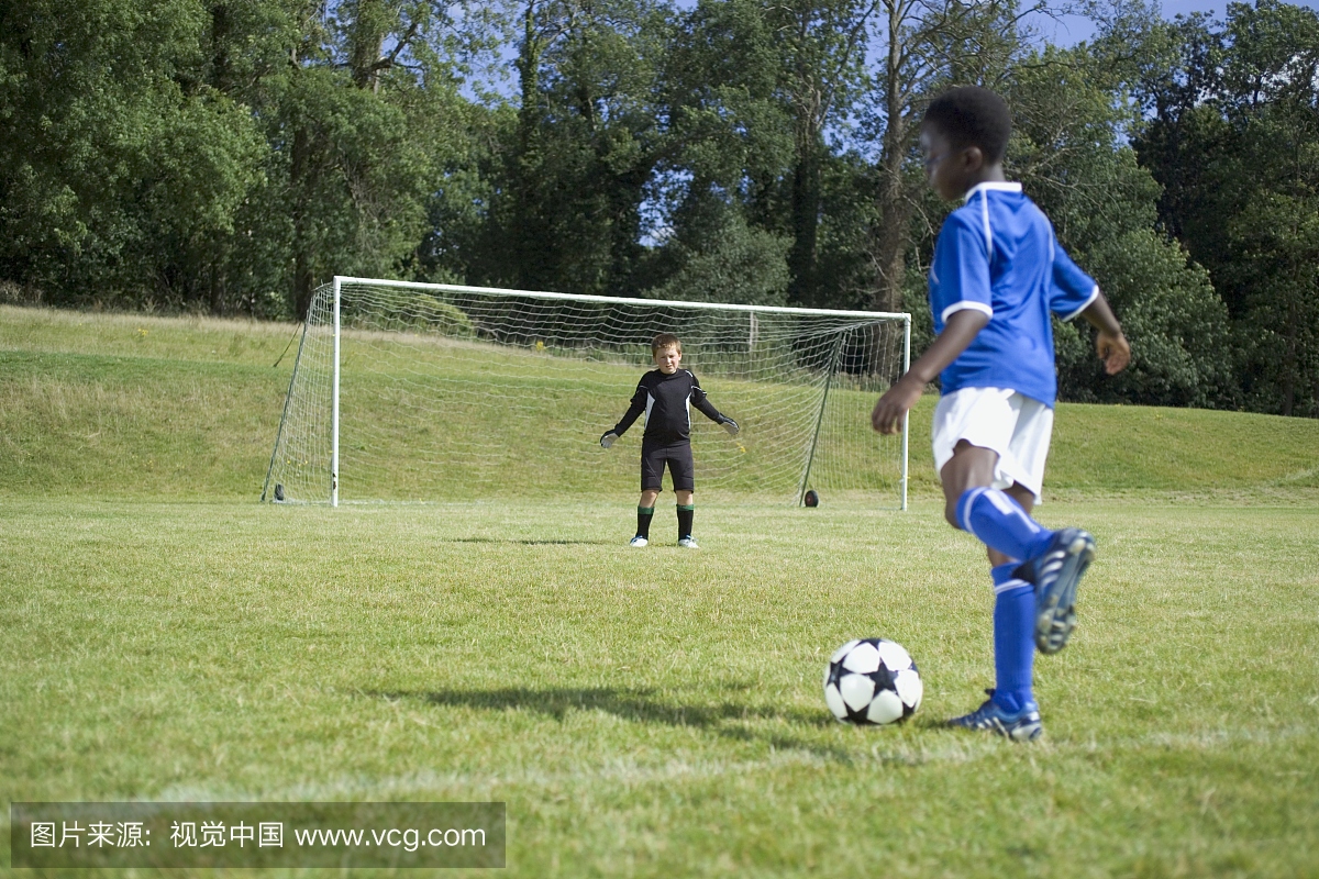 年轻的足球运动员准备踢球,守门员站在外面的