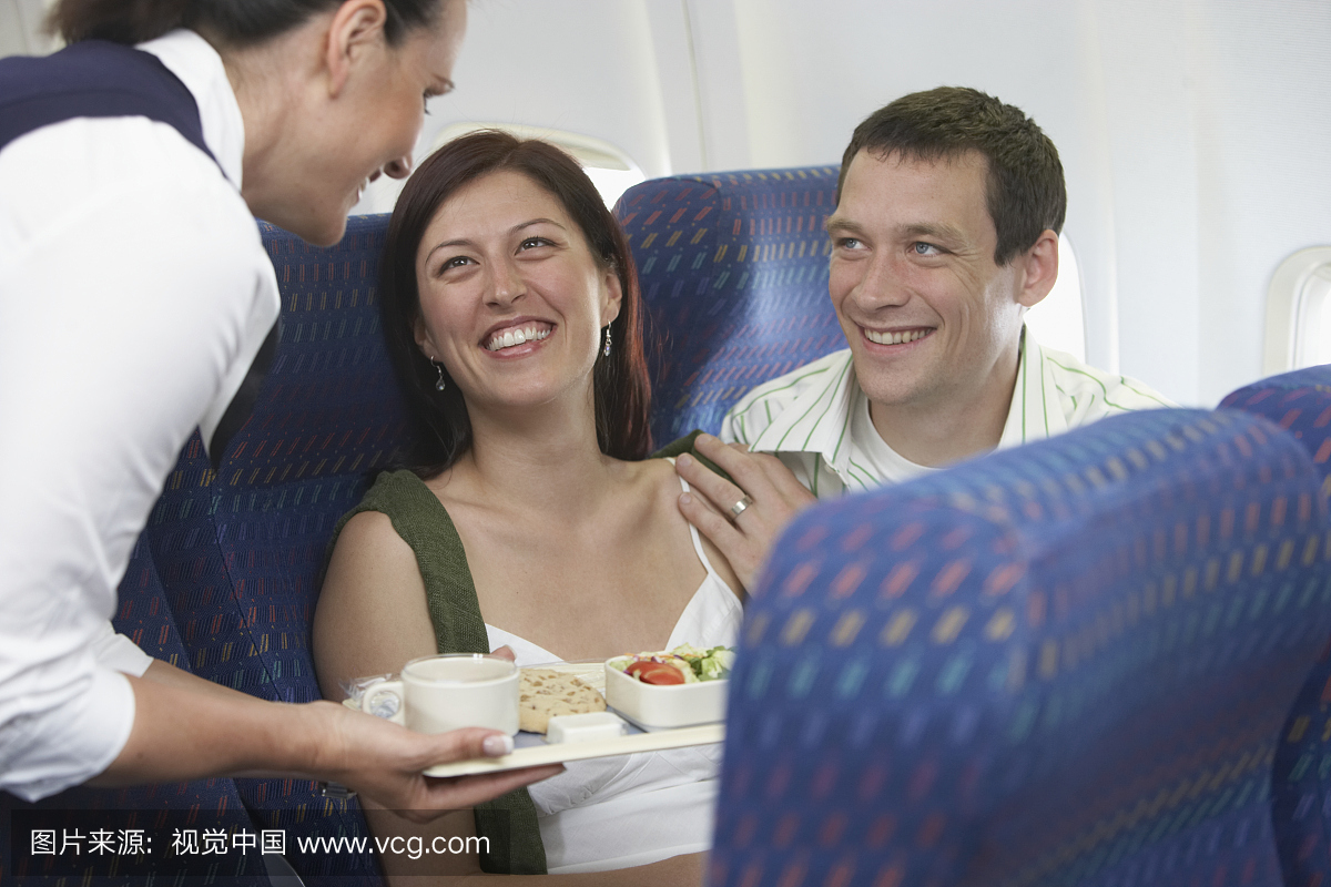 乘务员给飞机上的男人和年轻女子送餐