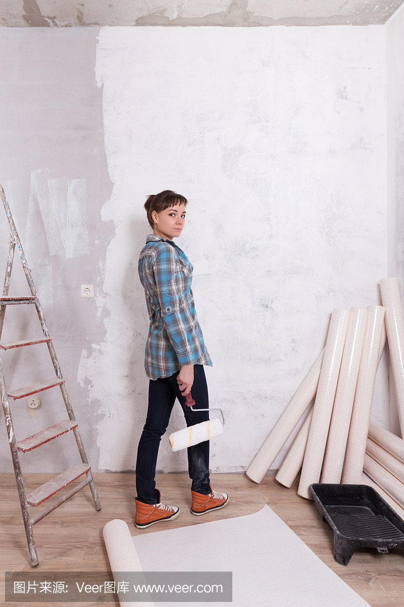 漂亮的女人与辊粘贴壁纸修理房子