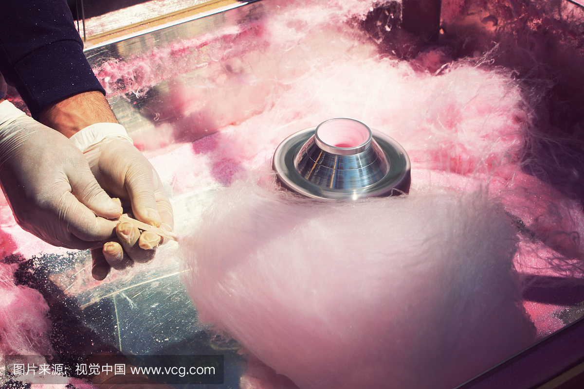 一个人在乳胶手套,在棍子上制作粉红色的棉花