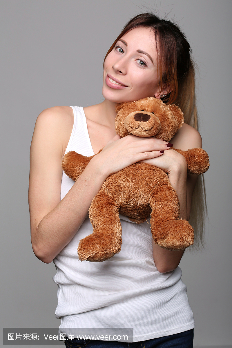 单身女孩拥抱泰迪熊。特写。灰色背景