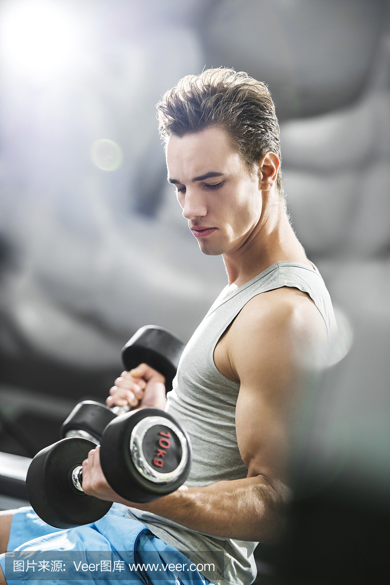男子在健身房里用哑铃锻炼身体。