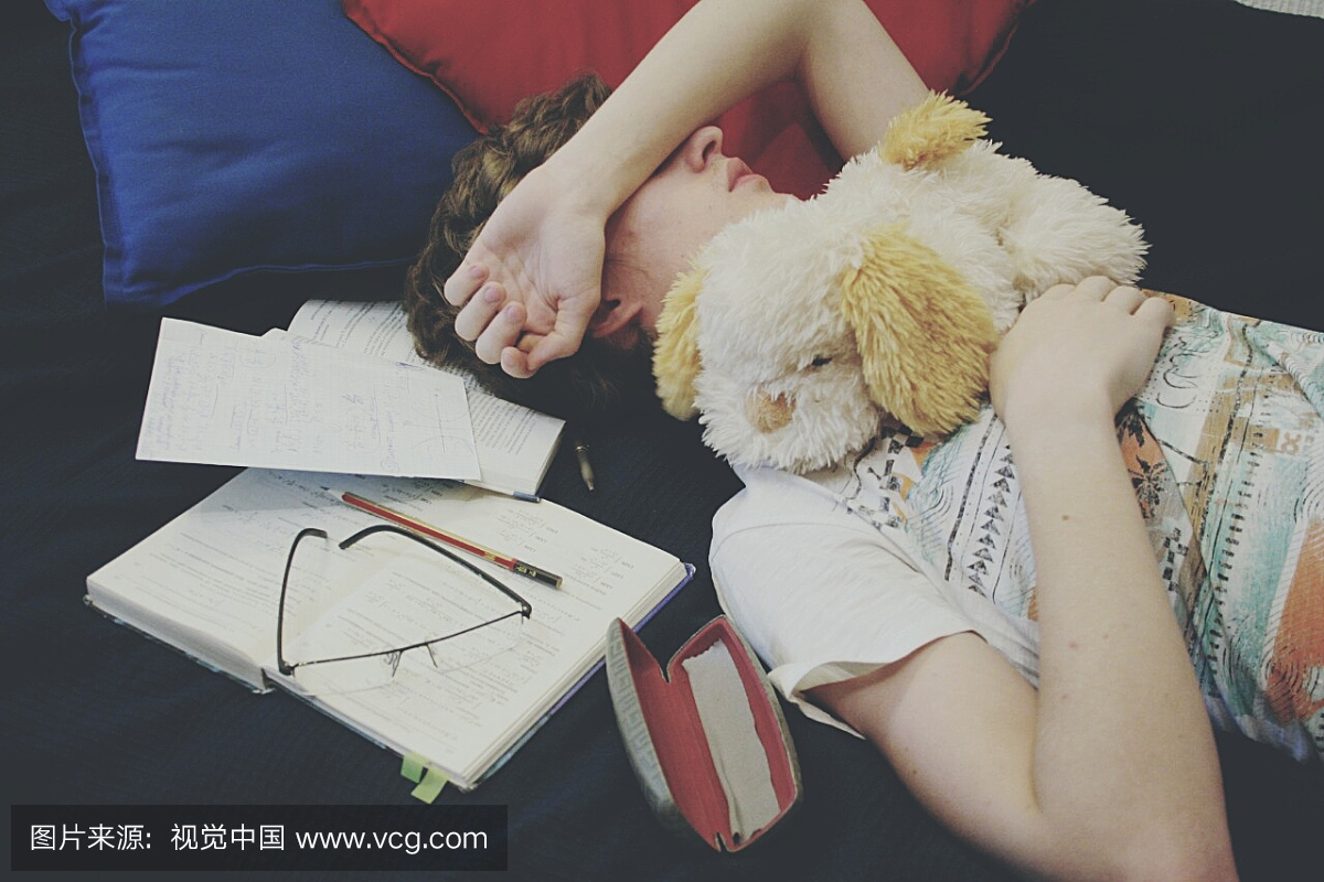十几岁的男孩在家里躺在床上睡觉的书和毛绒玩