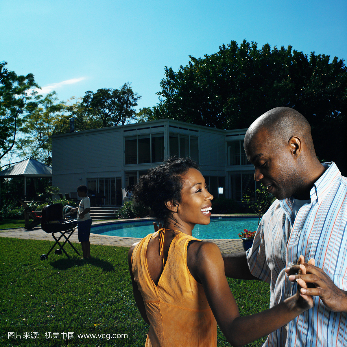 中间的成年夫妇微笑着和在游泳池后面的花园里