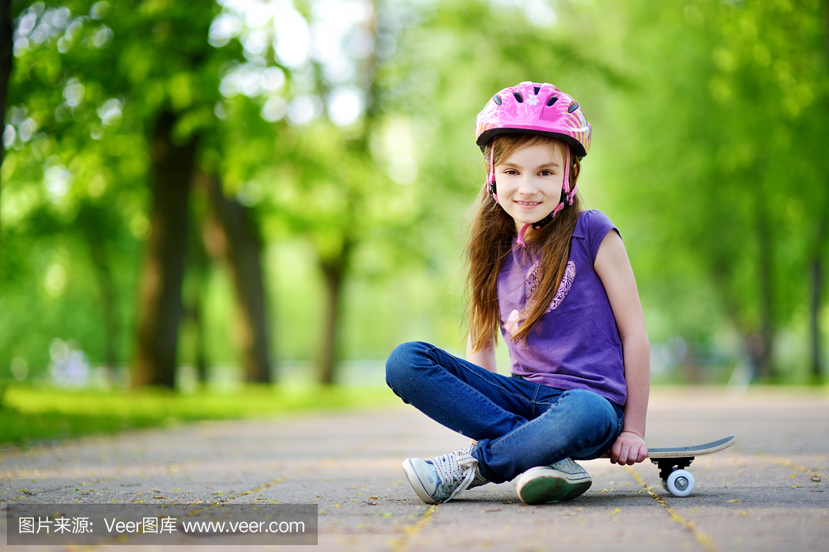 可爱的小青春期前女孩戴着头盔坐在滑板上