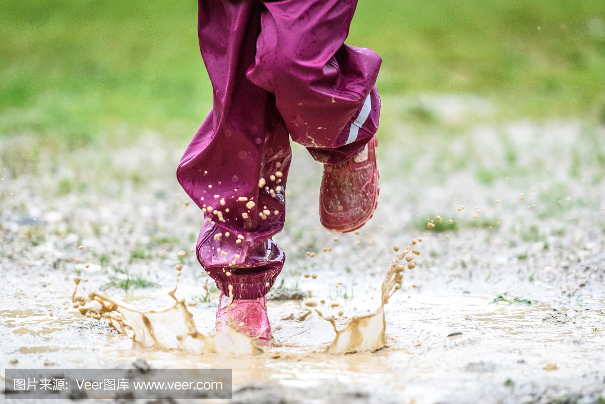 儿童在橡胶靴和雨衣在水坑中跳跃。