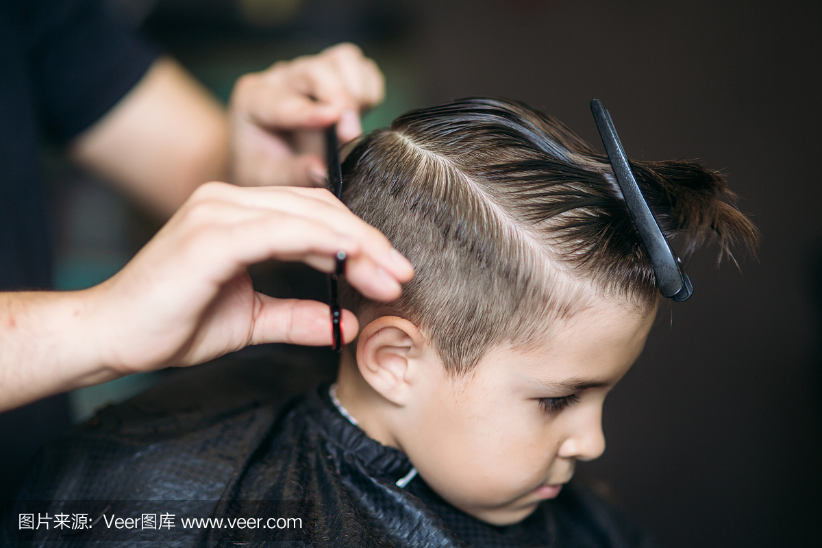 小男孩在理发店坐在椅子时由理发师理发。