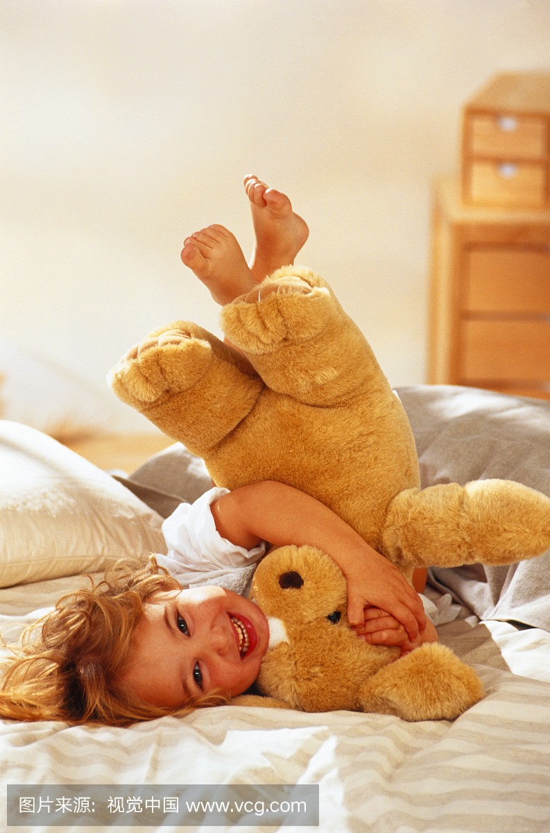 年轻的女孩(1-3岁)和玩具熊在床上玩