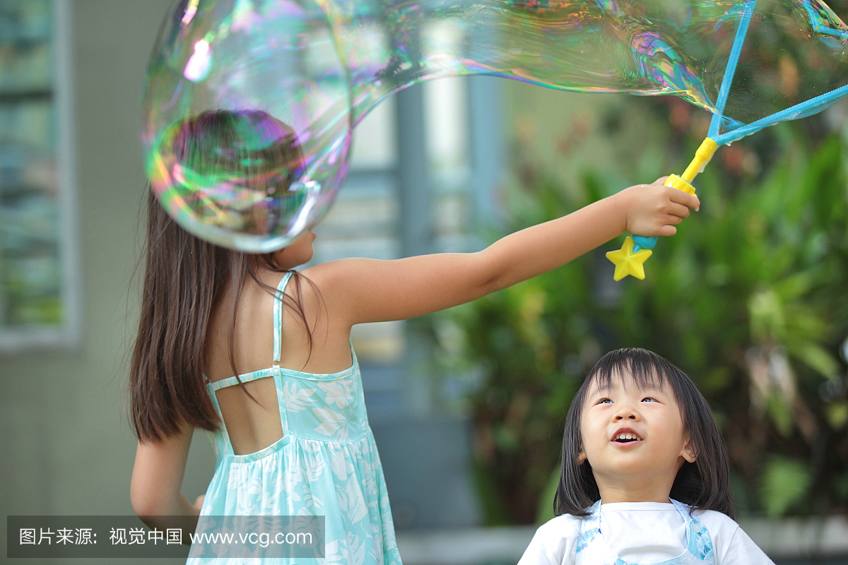 小女孩和她姐姐在花园里玩巨大的泡沫。
