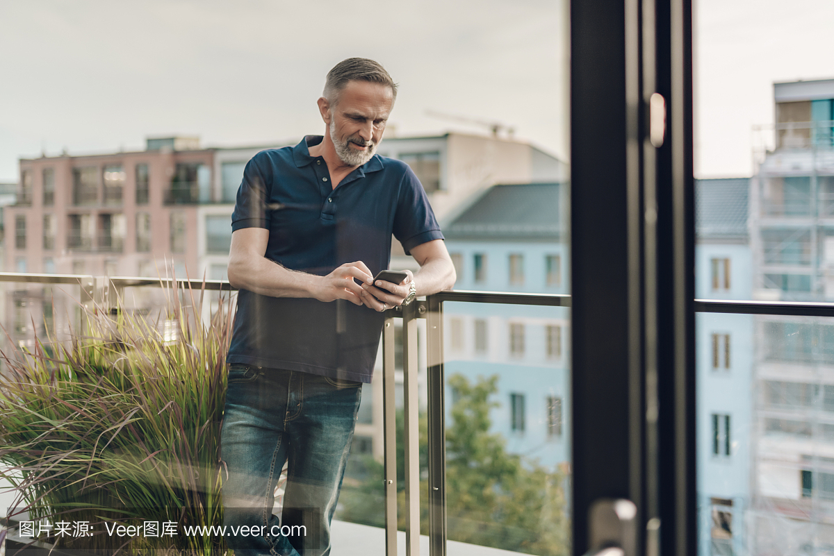 英俊胡子的中年男子在柏林的阳台上看着手机