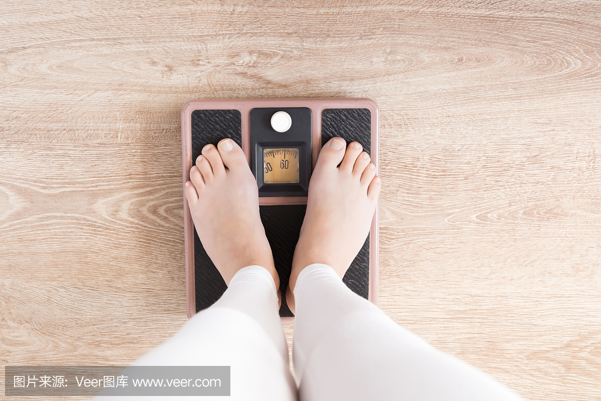赤脚站在体重秤上的女人。新的健康营养开始,