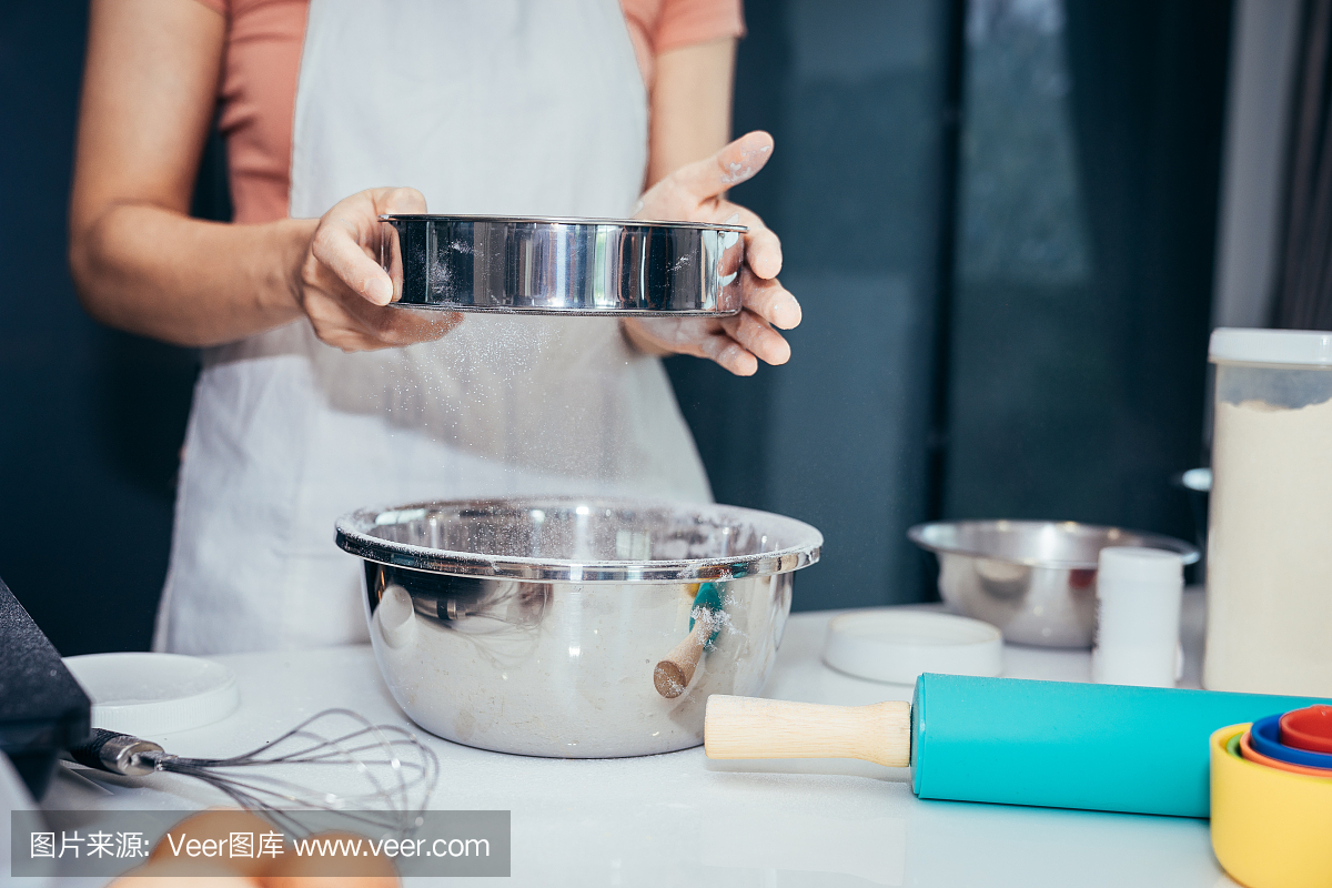 一位女士将面粉筛入不锈钢碗中。女孩正在筛面