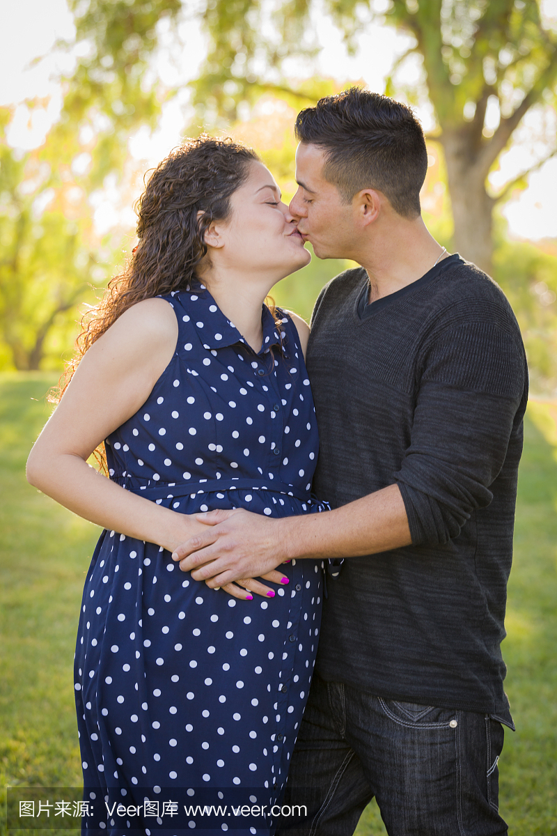 西班牙裔男子在公园里户外亲吻怀孕的妻子