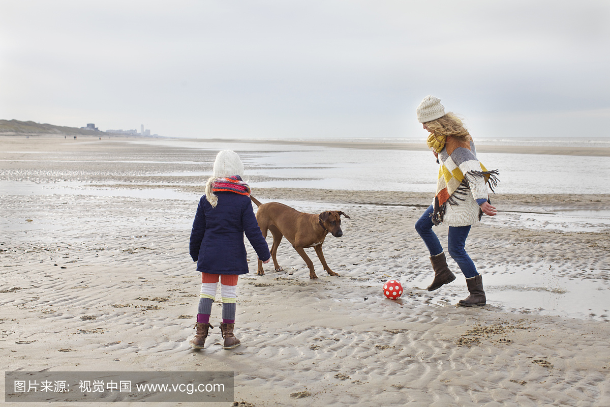中旬成年女子与女儿和狗在沙滩上踢足球,Bloe