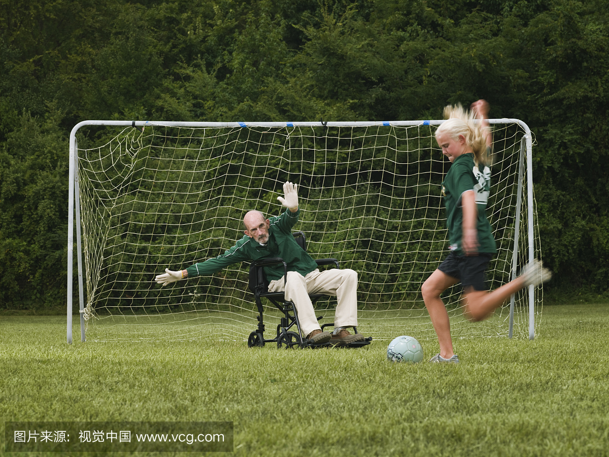 女孩(10-11)和爷爷在轮椅上踢足球作为守门员