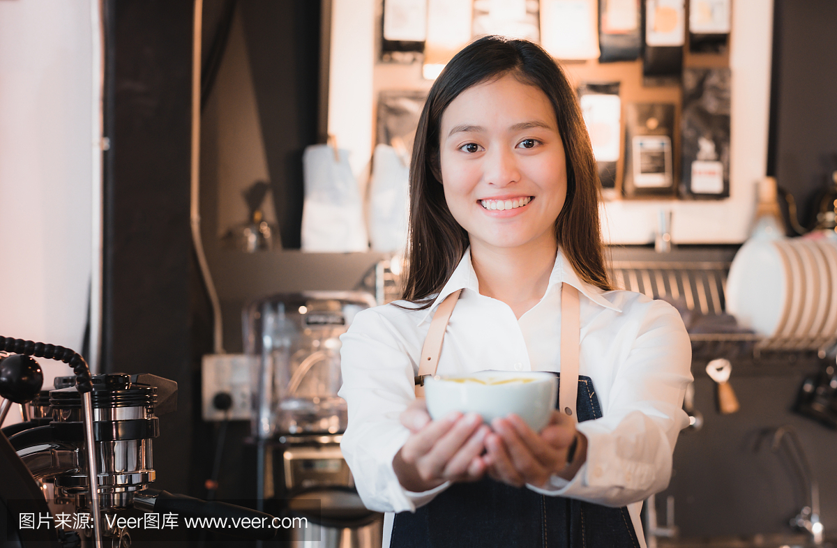 亚洲女人咖啡师穿牛仔围裙拿着热咖啡杯送达顾