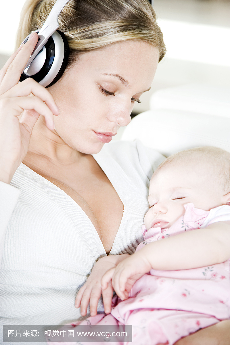 母亲在耳机上听音乐,而宝宝睡觉