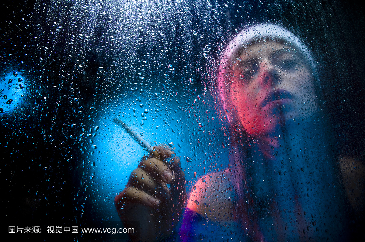 女人拿着香烟和吸烟背后湿,阴雨的窗户