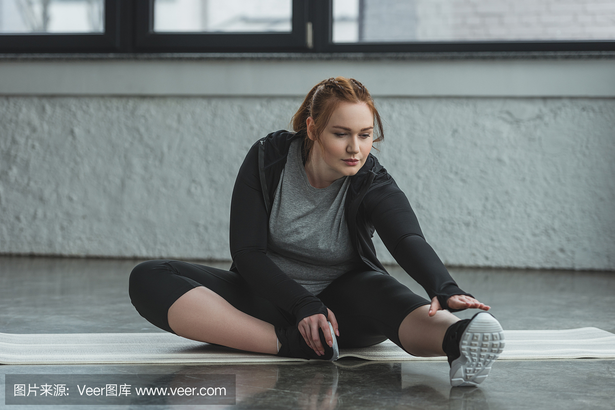 肥胖的女孩伸展在健身房的地板上