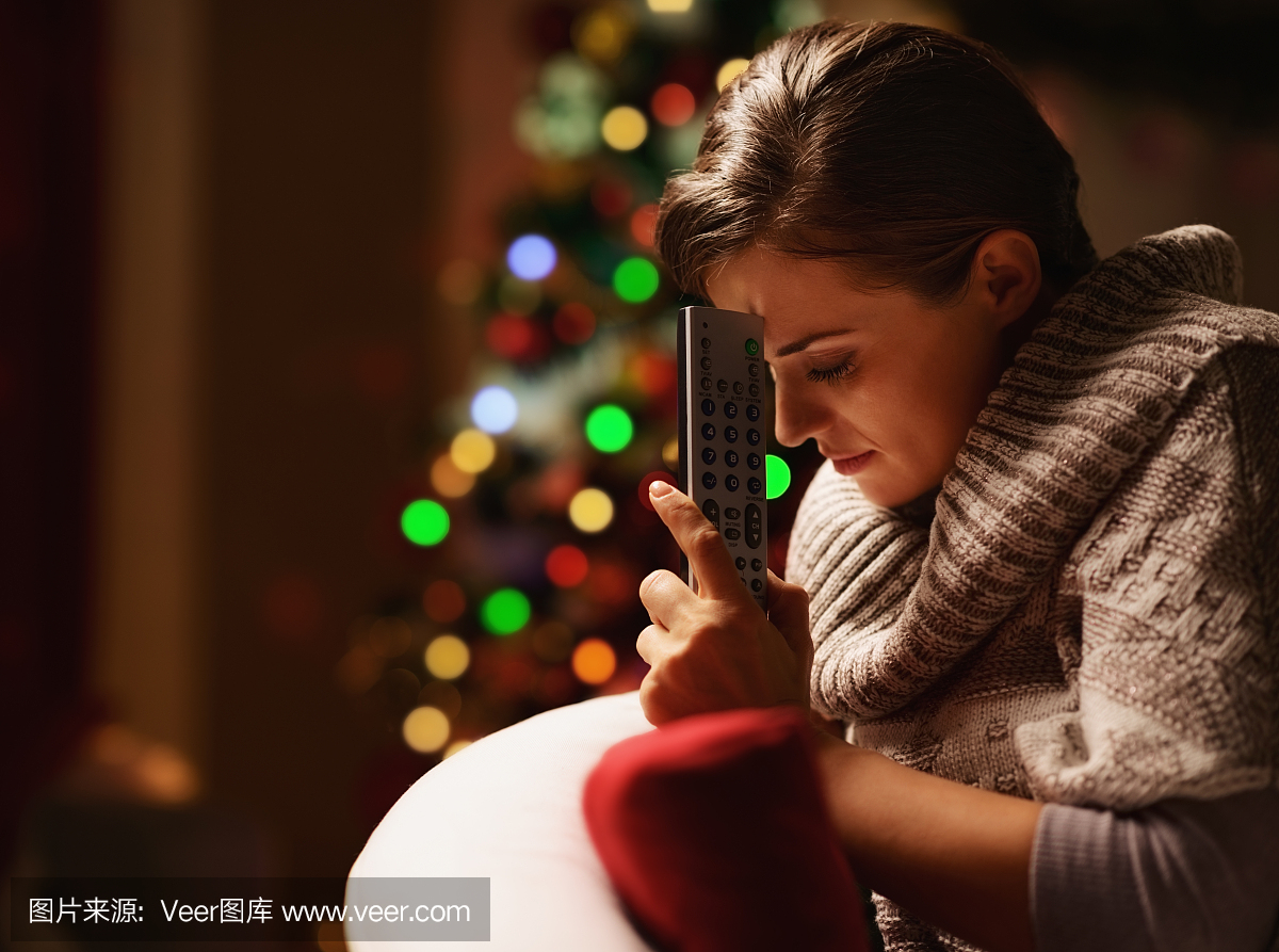 沮丧的女人与电视遥控器附近的圣诞树