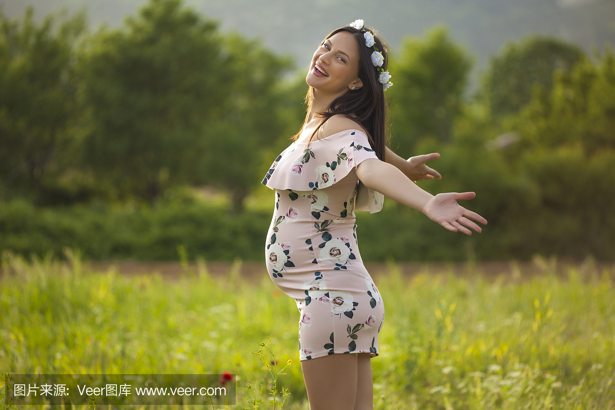 在她的头上的鲜花花圈草地上的快乐孕妇