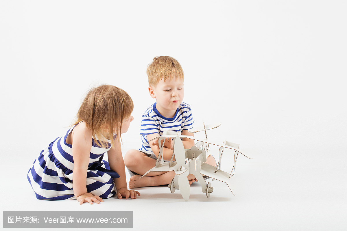 小孩玩纸玩具飞机坐在白色背景下的地板上。