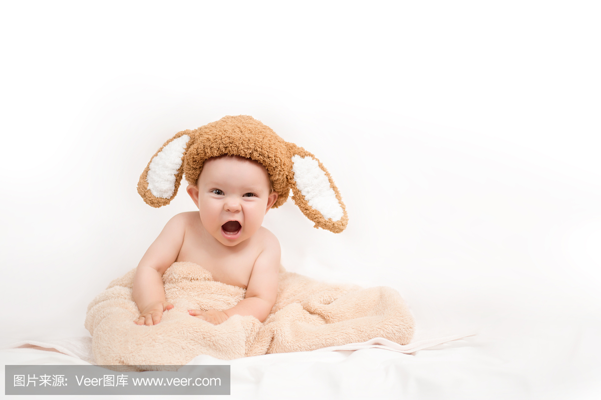 一个可爱的小宝宝戴着兔子帽子坐在白色的床上