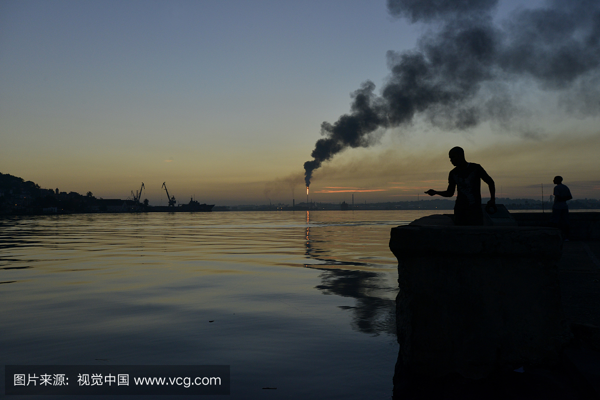 在哈瓦那湾钓鱼的男子与吸烟炼油烟囱在远处。