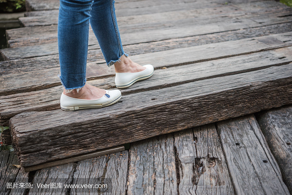 妇女的腿服装蓝色牛仔裤和白色的鞋站在木地板