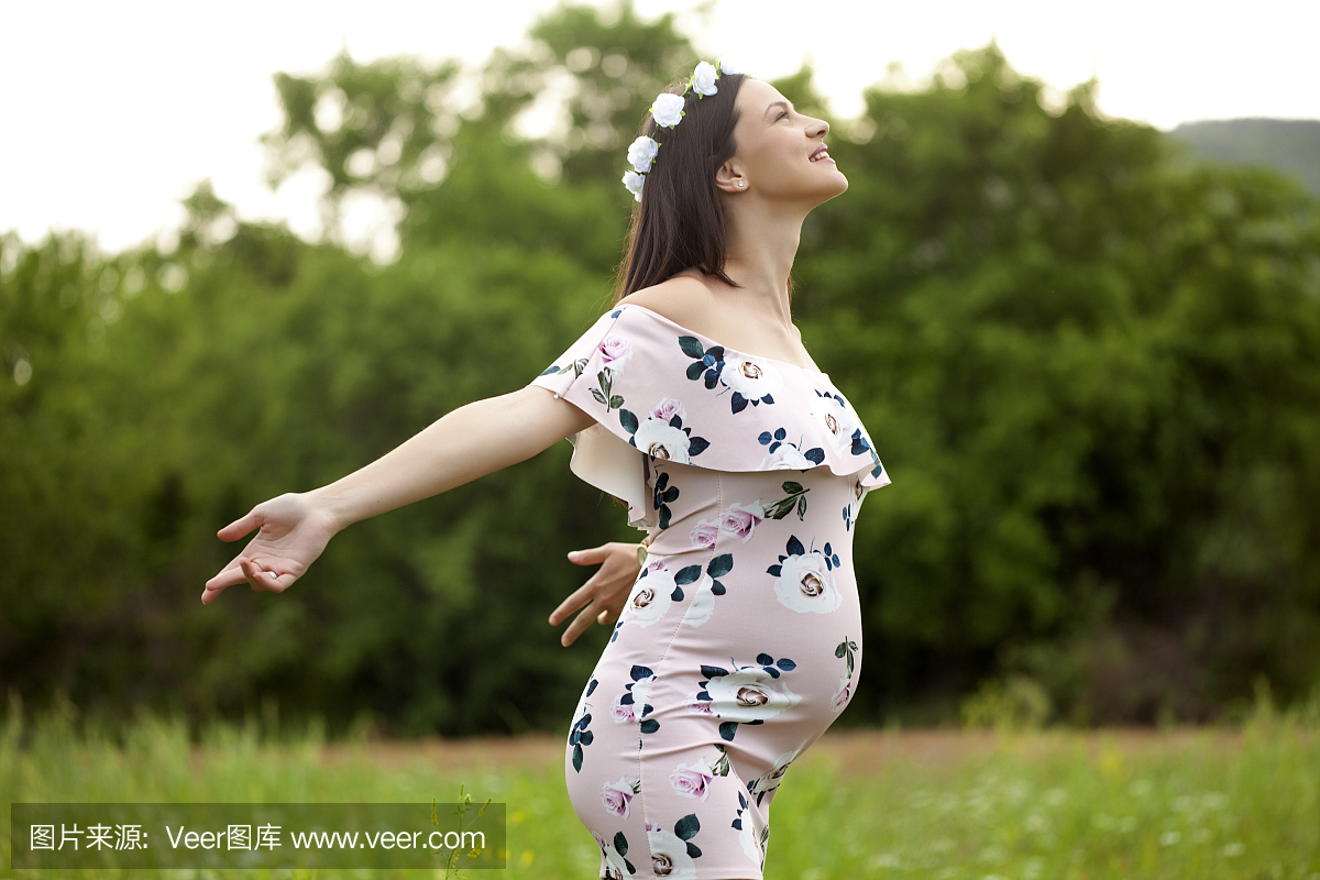 在她的头上的鲜花花圈草地上的快乐孕妇