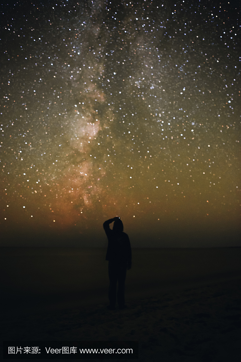 一个孤独的人站在海滩上,看着银河系的满天星
