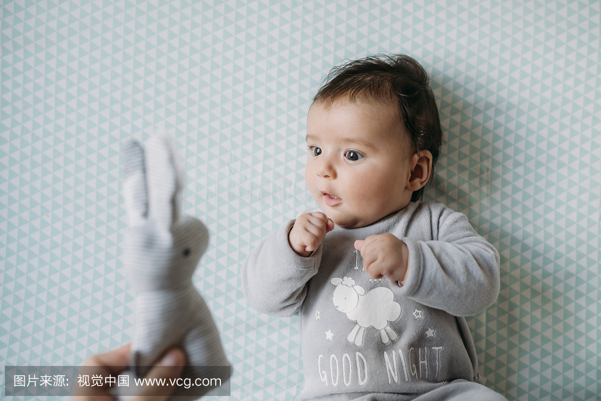 躺在婴儿床上的小女孩看着拿着玩具兔子的手