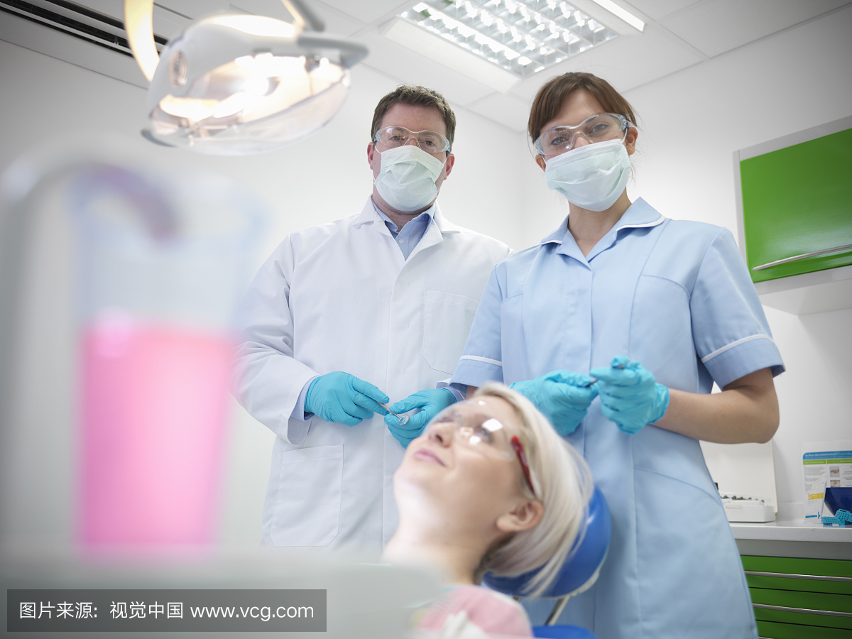 牙医和学徒佩戴安全眼镜和面具与患者在牙科手