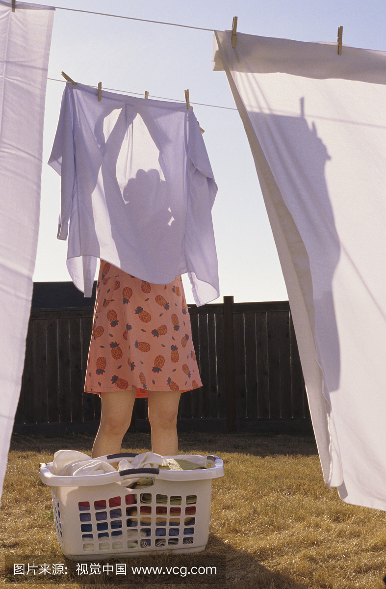 成熟的女人在洗衣线上挂衬衫,用脚踩篮
