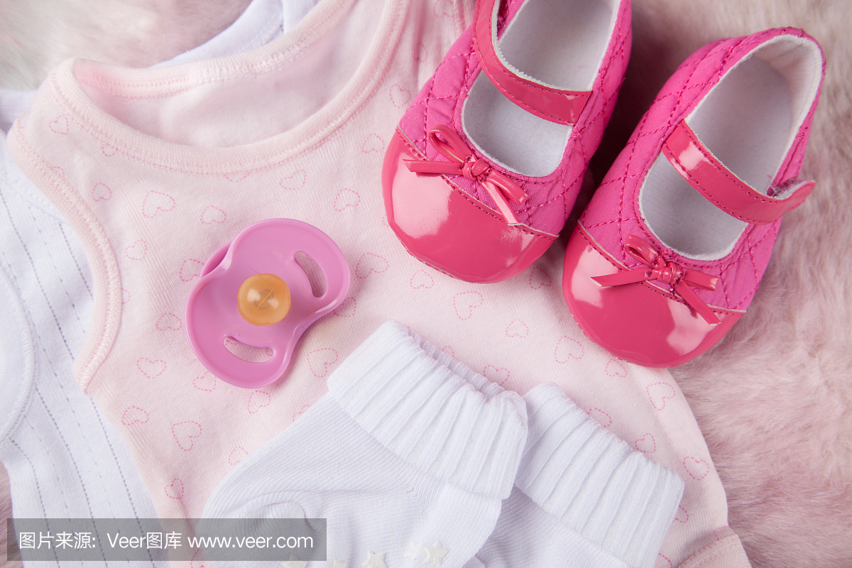 在柔软的粉红色毛皮背景上的女婴服装
